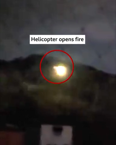 Nighttime scene showing a bright flash of light in the sky, circled in red, with the caption ‘Helicopter opens fire.’