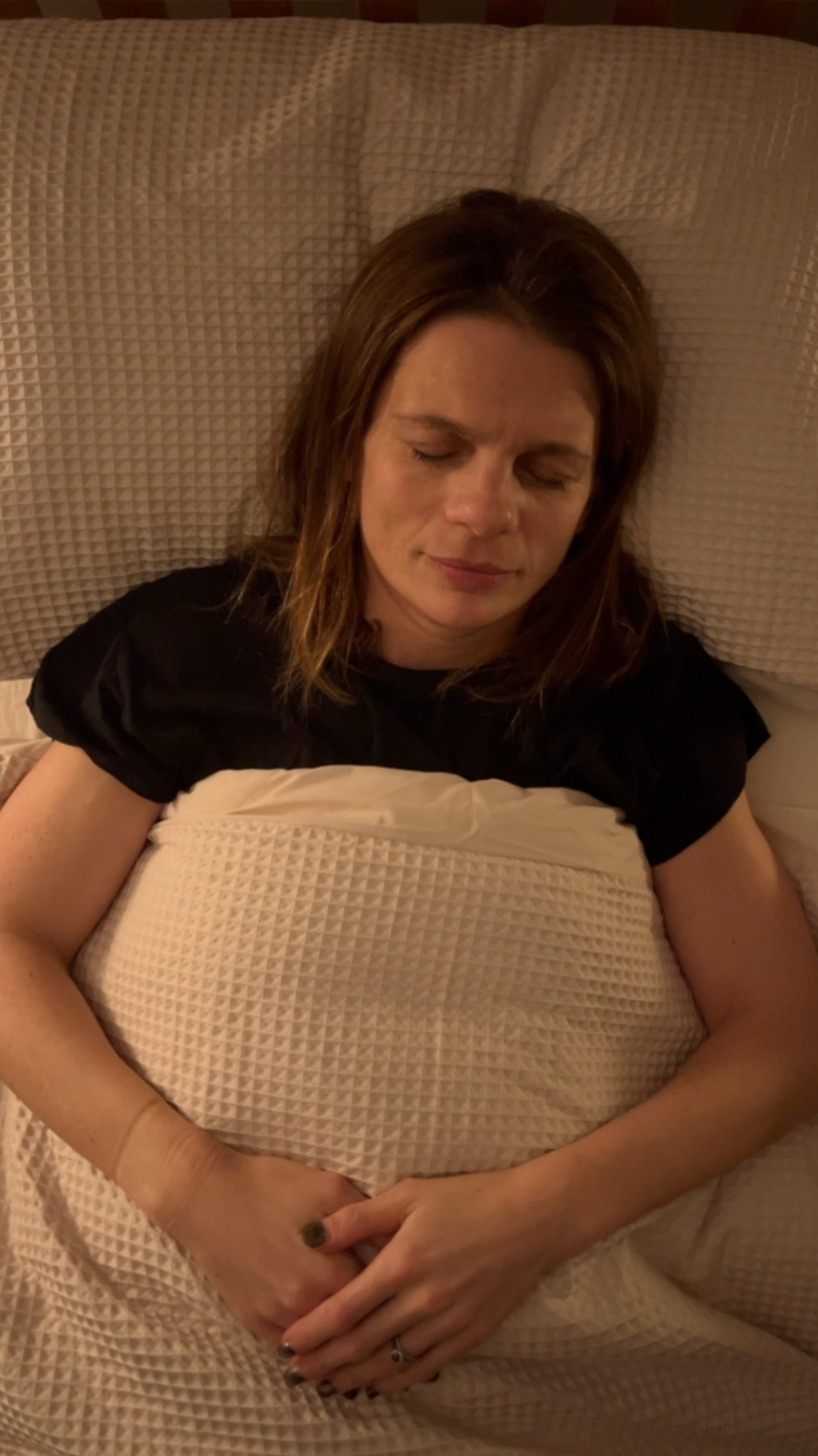 A birds eye view image of BBC reporter Ruth Clegg in bed with a white duvet on a white pillow and with her eyes shut