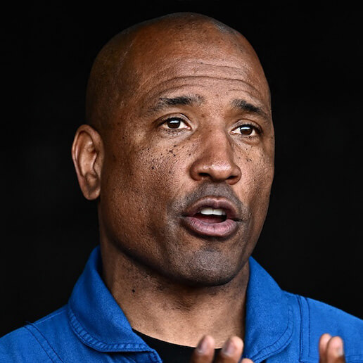 A headshot of Orion's pilot Victor Glover. He is a middle-aged black man, bald head, caught mid-conversation with his brow furrowed as he answers a question.