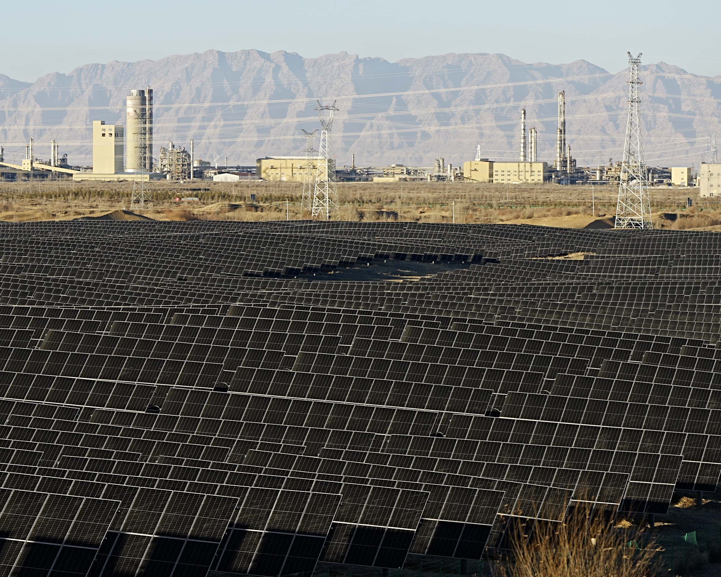 內蒙古沙漠中的太陽能板,遠處可見發電廠與群山背景