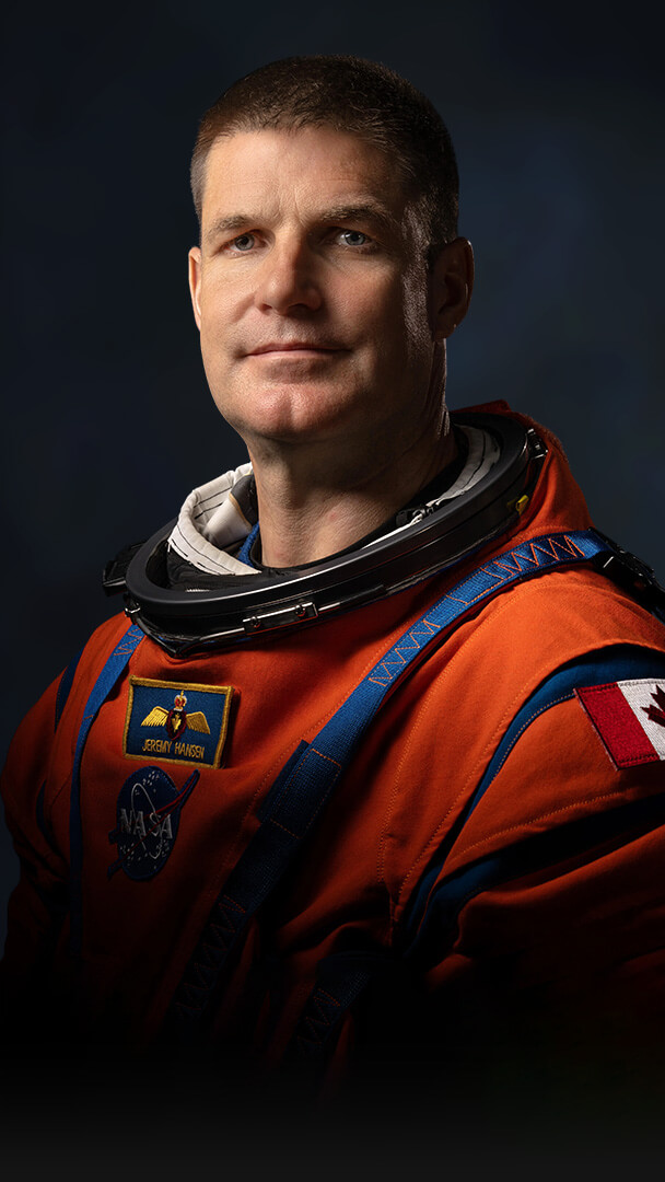 Official Nasa portrait of Jeremy Hansen in his orange spacesuit showing him from mid-waist. With short hair and a cleft chin, he is clearly a big man and, perhaps, looks a little uncomfortable having his photo taken.