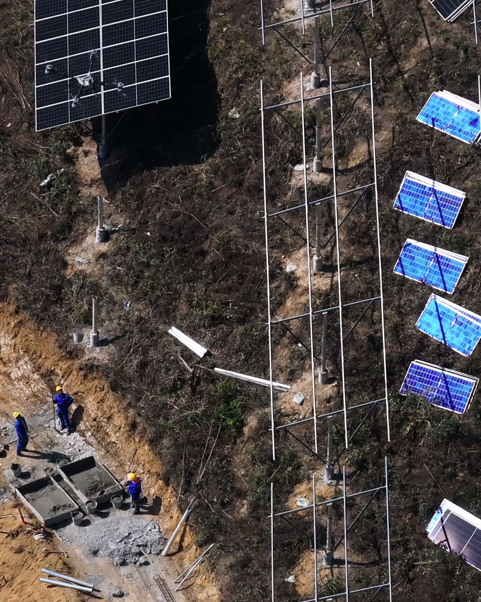 航拍畫面顯示,戴著黃色安全帽的工人在山坡一條泥土壕溝旁安裝太陽能設備。坡面上已架起一排排金屬支架與多塊藍色太陽能板,附近還放置著更多面板與支撐架。