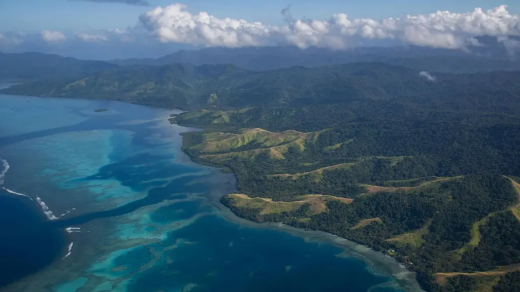 A man walks along a row of bright green crops, towards tree covered hilltops (Credit: Frankie Adkins)