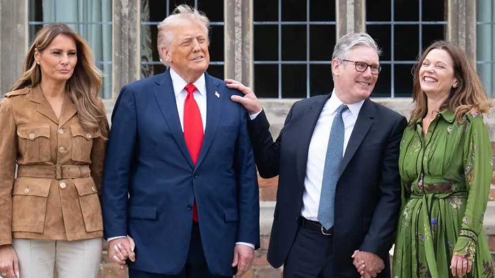 UK Prime Minister Sir Keir Starmer wears a dark suit over a white shirt and blue tie as he laughs while placing a hand on the shoulder of US President Donald Trump, who is wearing a blue suit over a white shirt and red tie.