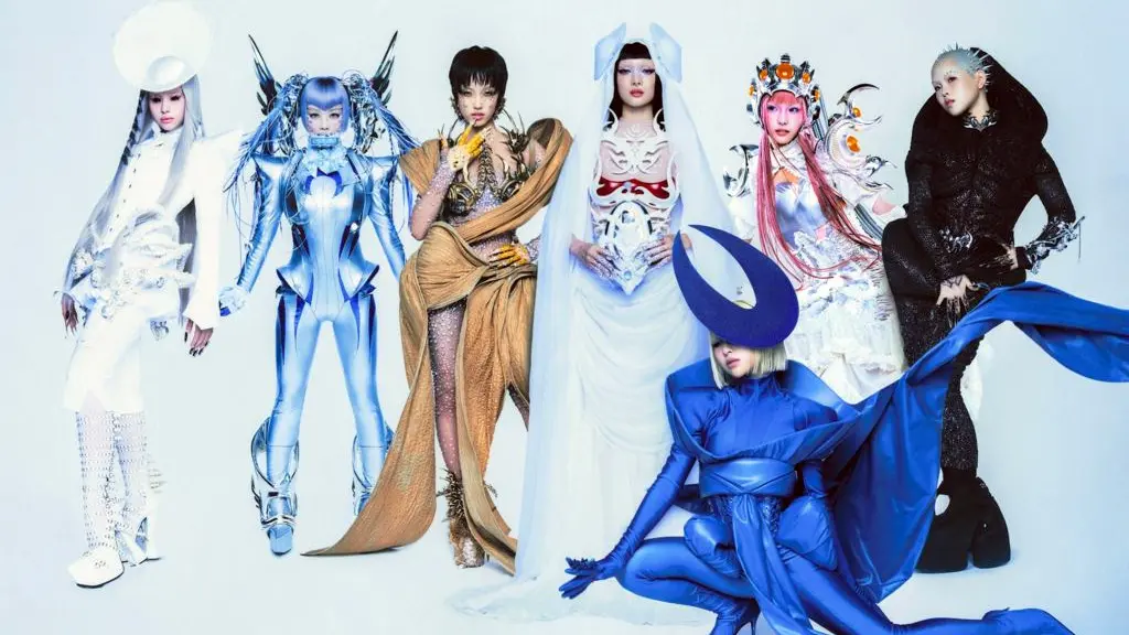 The seven members of XG pose for a promotional photo in a triangular formation, weaing a variety of pastel shaded, Victorian-inspired outfits