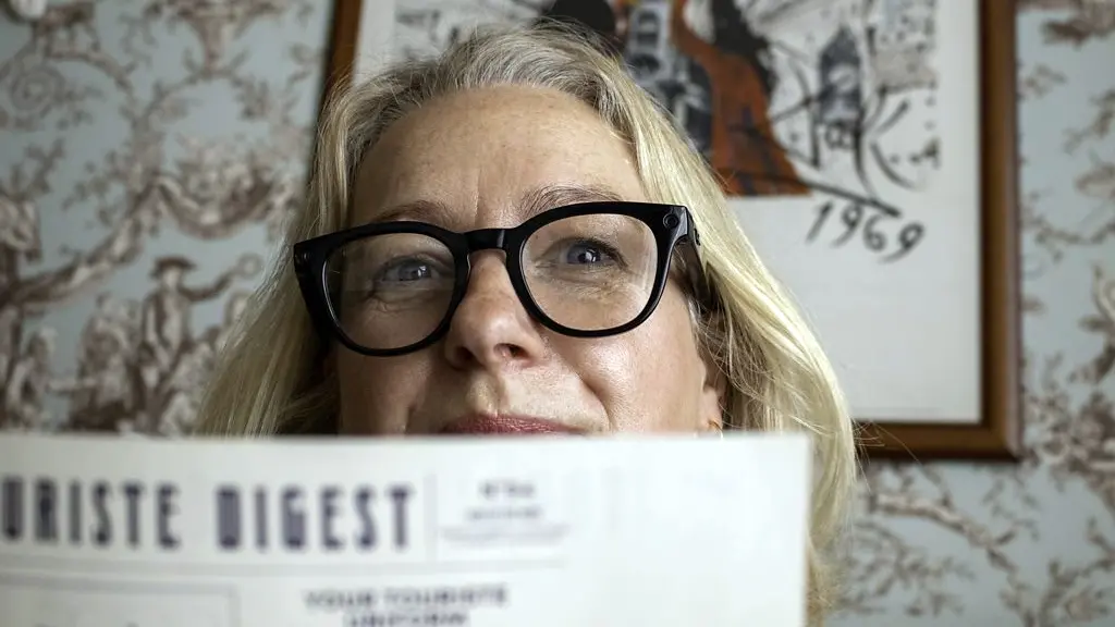 A woman wearing black-framed glasses peers over an orange menu in a cafu00e9 (Credit: Laura Hall)