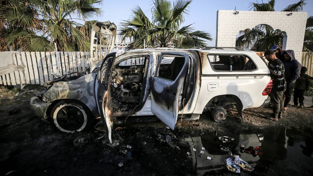 Palestinians are standing next to a destroyed vehicle in Deir Al-Balah, in the central Gaza Strip