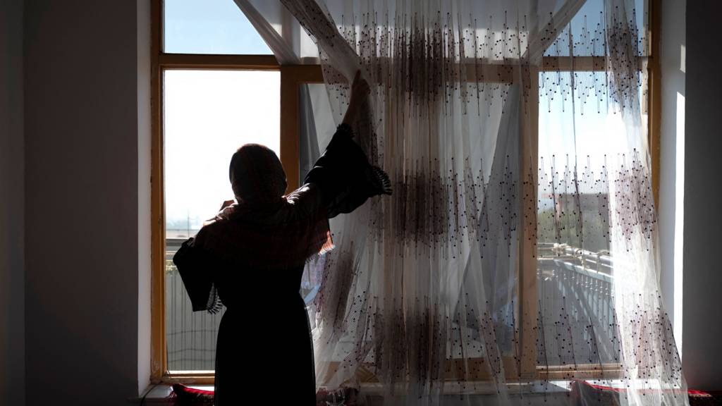 A 16 year old girl adjusts the curtains of a window in a house in Charikar, Afghanistan