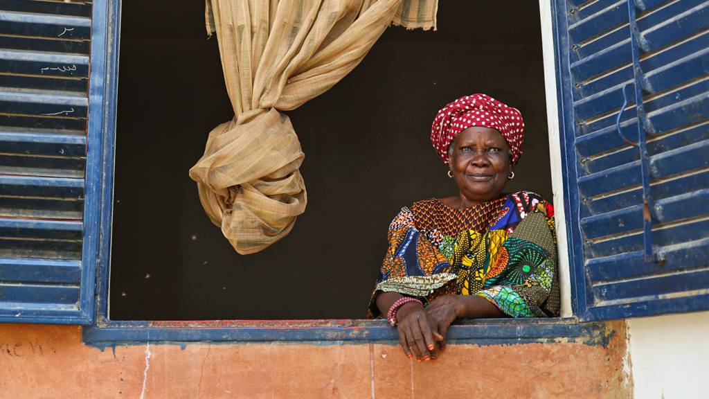 A woman looking out of a window with shutters in Touba, Senegal - March 2024