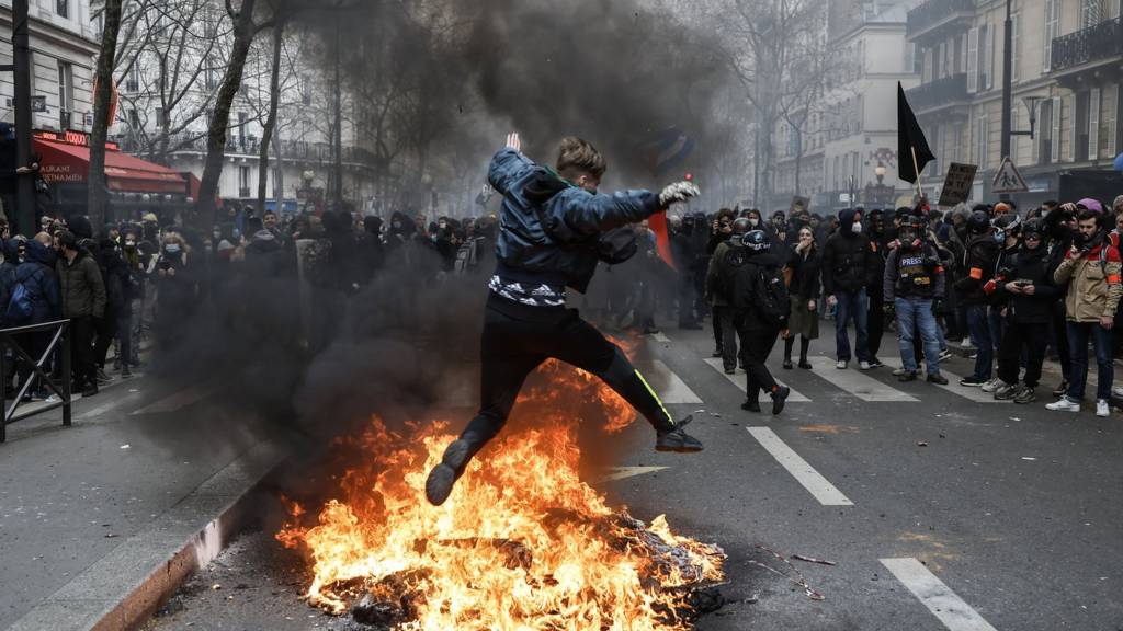 A protester jumps over burning debris in Paris