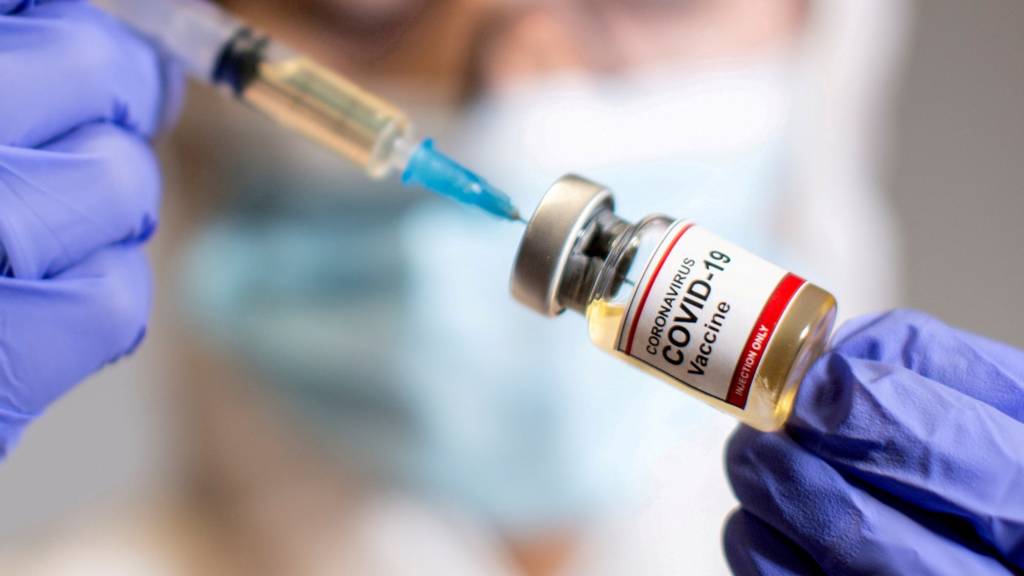 A woman holds a small bottle labeled with a Coronavirus COVID-19 Vaccine sticker and a medical syringe