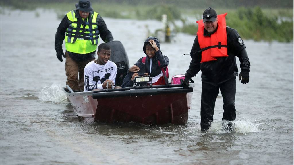 Children in boat with rescuers pulling them through floodwaters