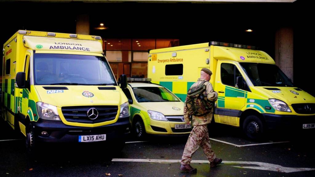 A man in military uniform walks past ambulances