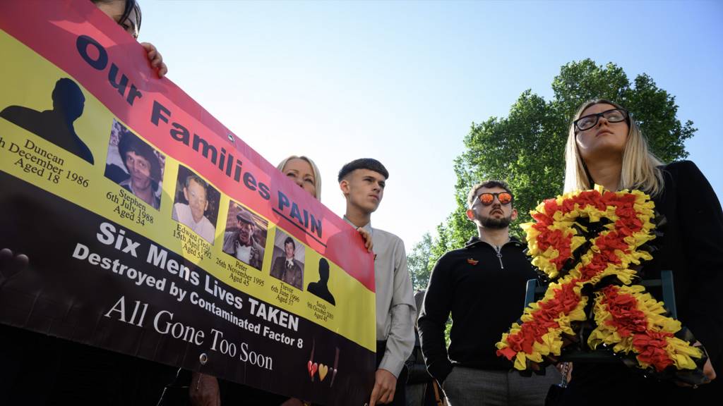 Families affected by the infected blood scandal hold a banner showing images of deceased relatives as they wait to enter the Methodist Central Hall to hear the findings of the six-year inquiry on May 20, 2024 in London, England