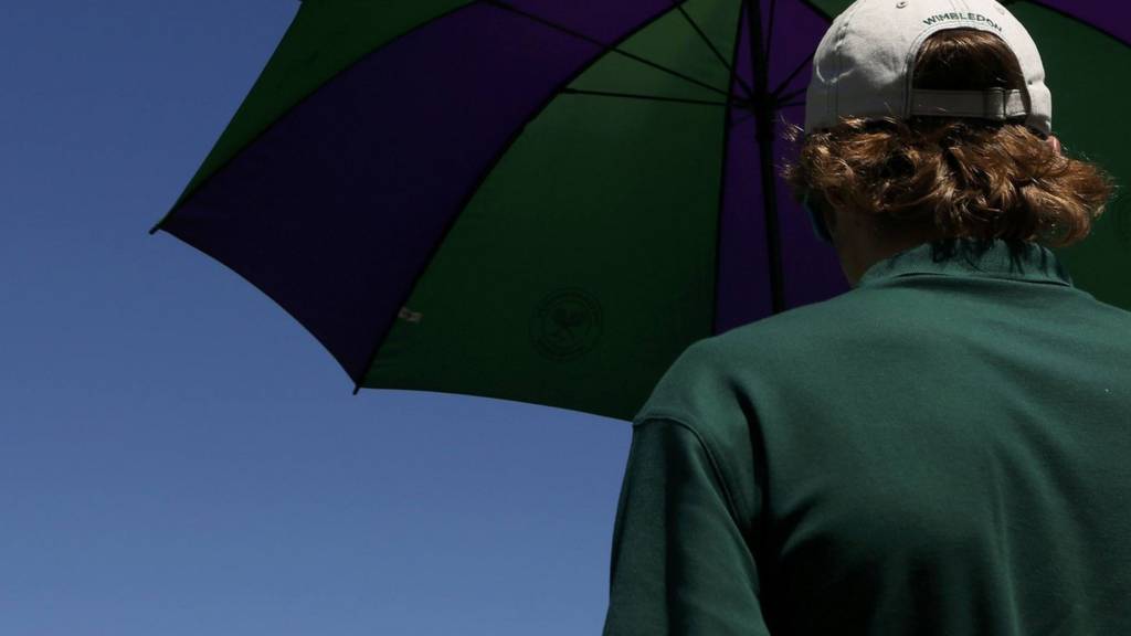 A ball boy shelters under an umbrella