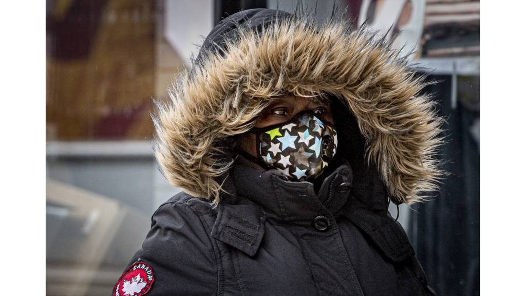 A woman wears a mask while waiting to get into a shop