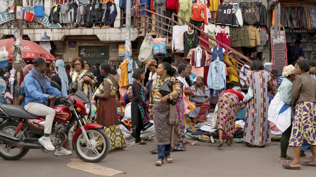 A man rides a motorcycle, as people buy and sell merchandise at the Birere market in Goma, North Kivu province, Democratic Republic of Congo, 29 December 2023