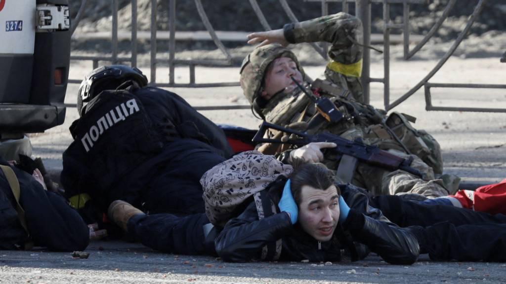 People take cover as an air-raid siren sounds, near an apartment building damaged by recent shelling in Kyiv, Ukraine February 26, 2022.