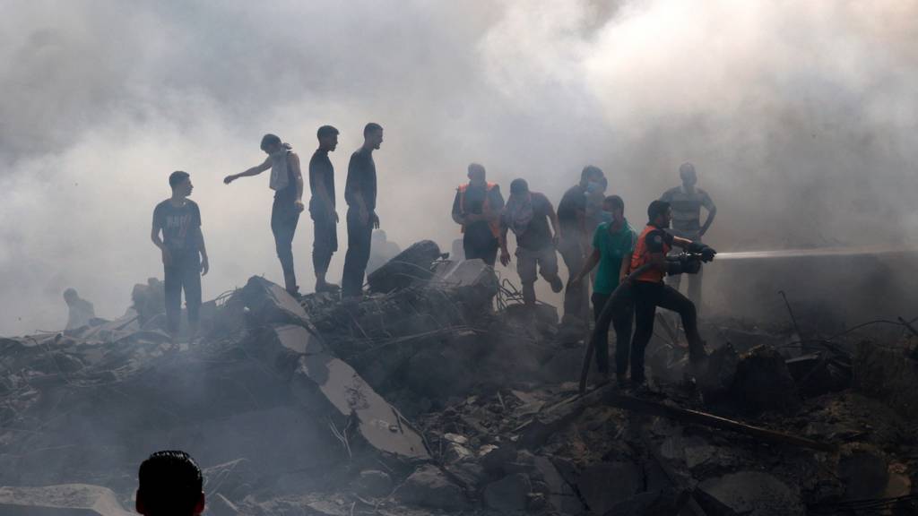 Palestinians stand on the rubble of a building as a civil defence worker uses a water hose following an Israeli strike in the southern Gaza Strip on 12 October 2023