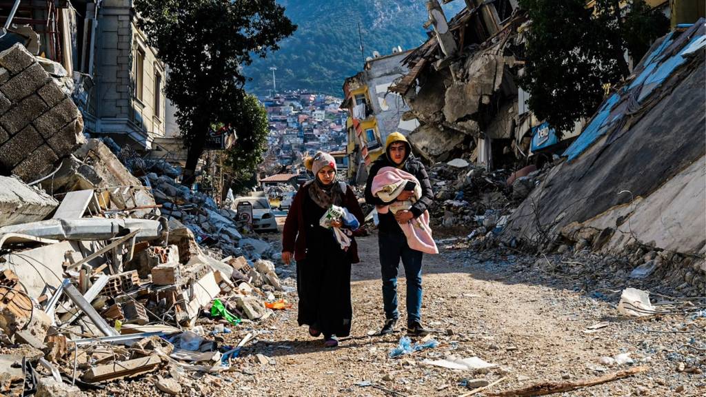 A woman and a man and a baby walk through the rubble in Hatay, Turkey