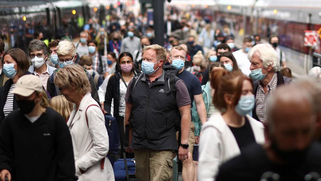 People wearing protective face masks walk along a platform at King's Cross Station, London