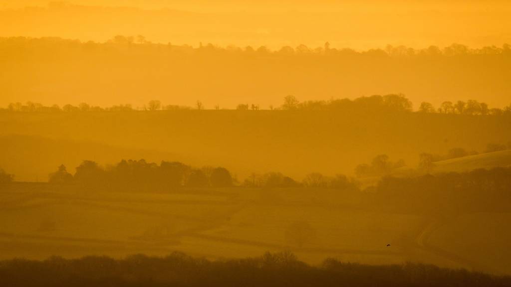 Tree lined ridges poke through the mist and fog as it hangs in valleys on the Mendip hills, Somerset at sunrise