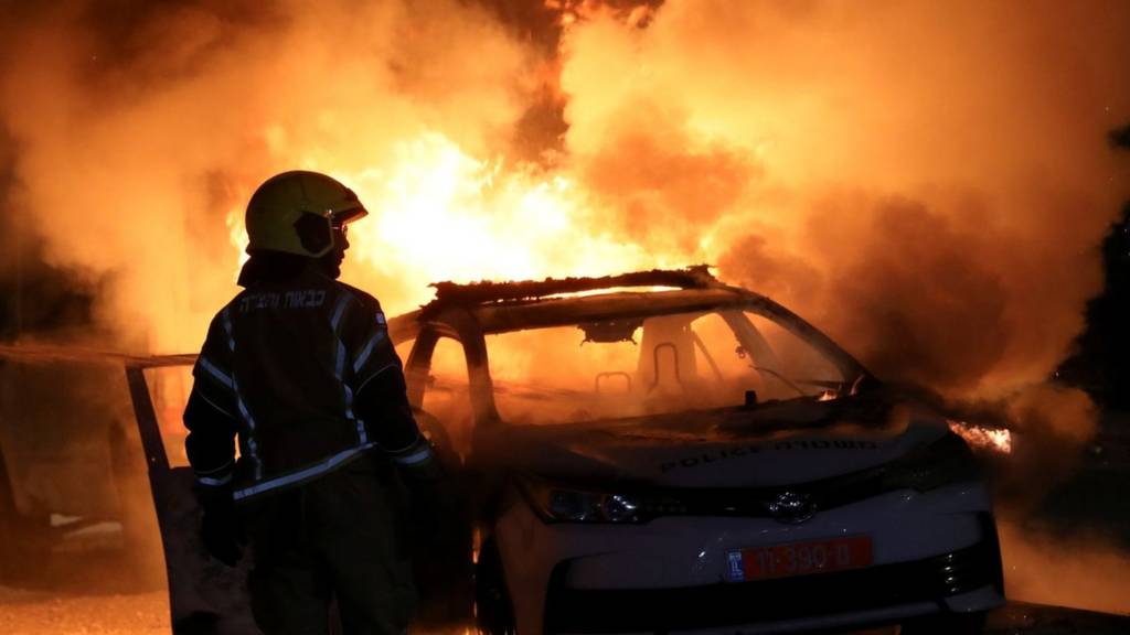 An Israeli firefighter stands near a burning Israeli police car during clashes between Israeli police and members of the country's Arab minority in the Arab Jewish town of Lod 12 May 2021