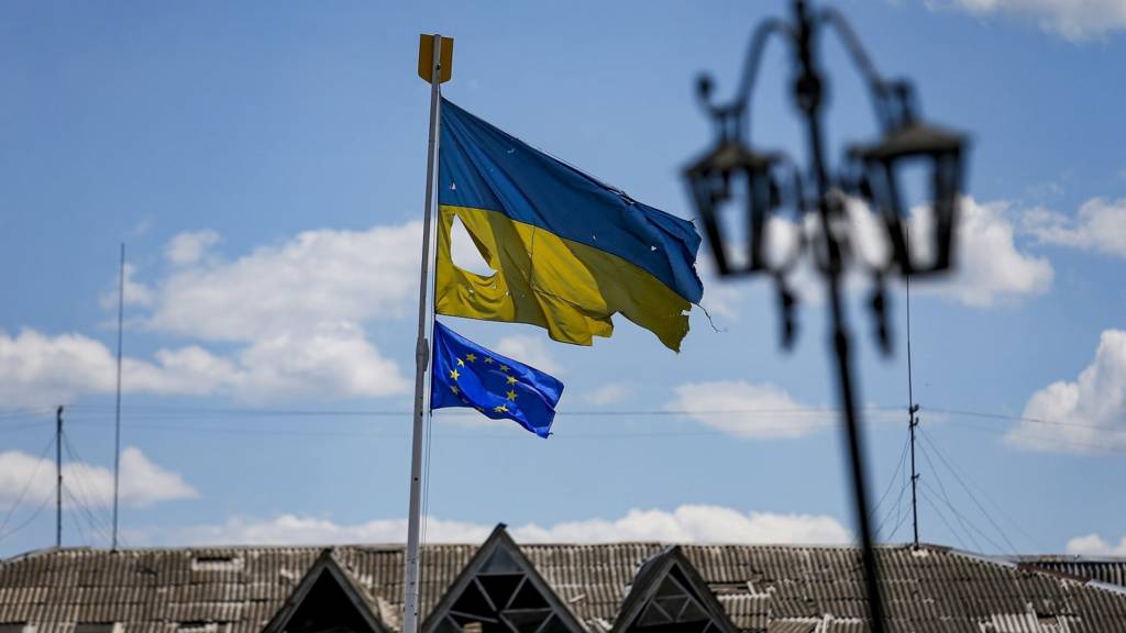 A flag of Ukraine ripped as a result of Russian shelling flies next to an EU flag in the central square of Malyn, Zhytomyr Region, northwestern Ukraine