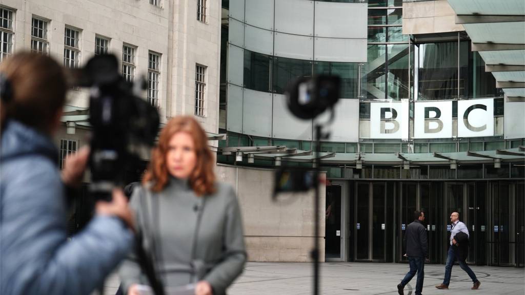 A broadcaster stands in front of a camera outside BBC Broadcasting House in central London