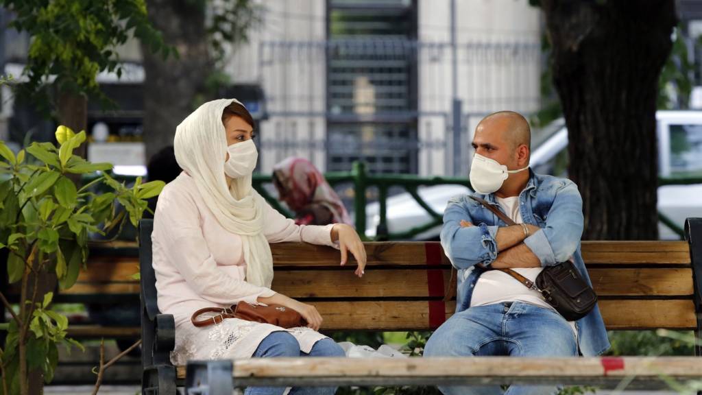 Iranian couple sitting on bench in masks