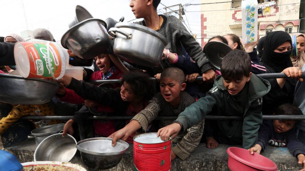 Palestinian children wait to receive food cooked by a charity kitchen amid shortages of food supplies, as the ongoing conflict between Israel and the Palestinian Islamist group Hamas continues, in Rafah, in the southern Gaza Strip, February 13, 2024.