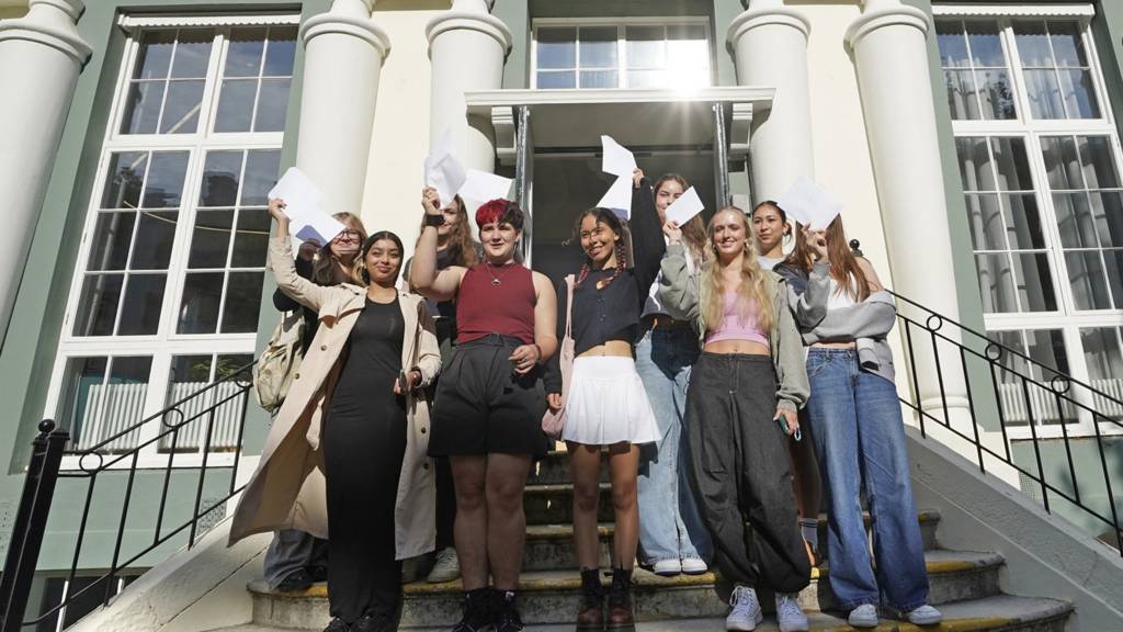 Students waving on steps with exam results outside a school in Brighton