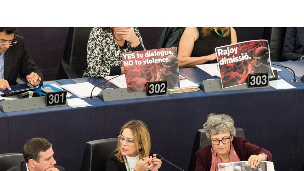 MEPs sitting with signs in front of their seats in the European Parliament