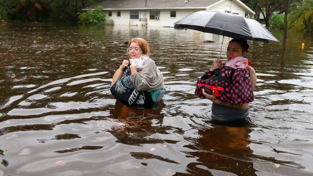 Two women wade through flood waters after having to evacuate their home when the flood waters from Hurricane Idalia inundated it on 30 August 2023 in Tarpon Springs, Florida