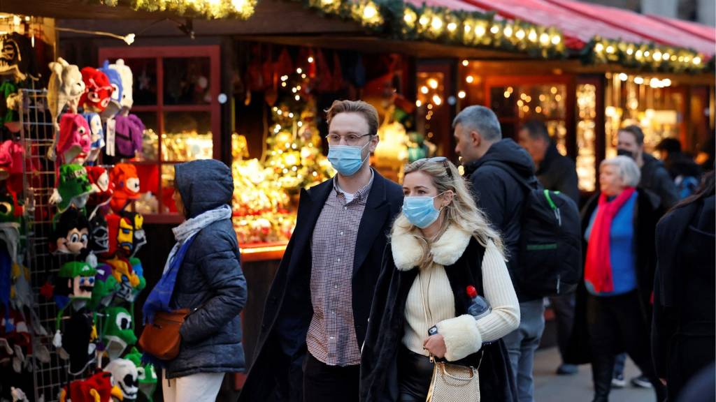 Shoppers, some wearing face coverings to combat the spread of Covid-19, walk past stalls at a Christmas market in central London on December 18, 2021