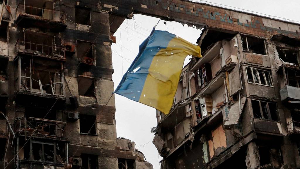 A torn flag of Ukraine hung on a wire in front a detroyed apartment building in Mariupol