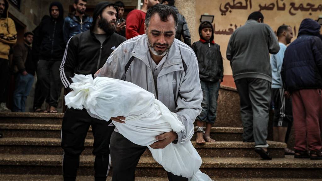 أبن يحمل ابنه الذي قتل في غارة إسرائيلية.