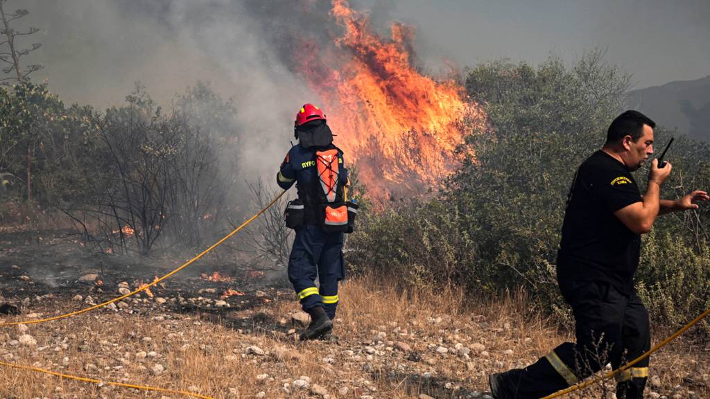 Firefighters and a civilian try to extinguish wildfires near the village of Vati, just north of the coastal town of Gennadi, in the southern part of the Greek island of Rhodes on 25 July 2023