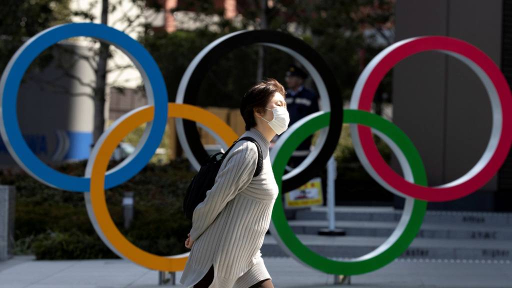 Woman in mask walks past Olympic rings