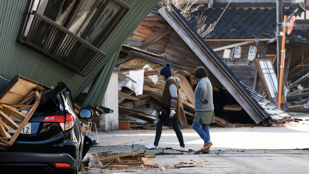 Residents walk past a damaged house, following an earthquake, in Nanao, Ishikawa prefecture, Japan
