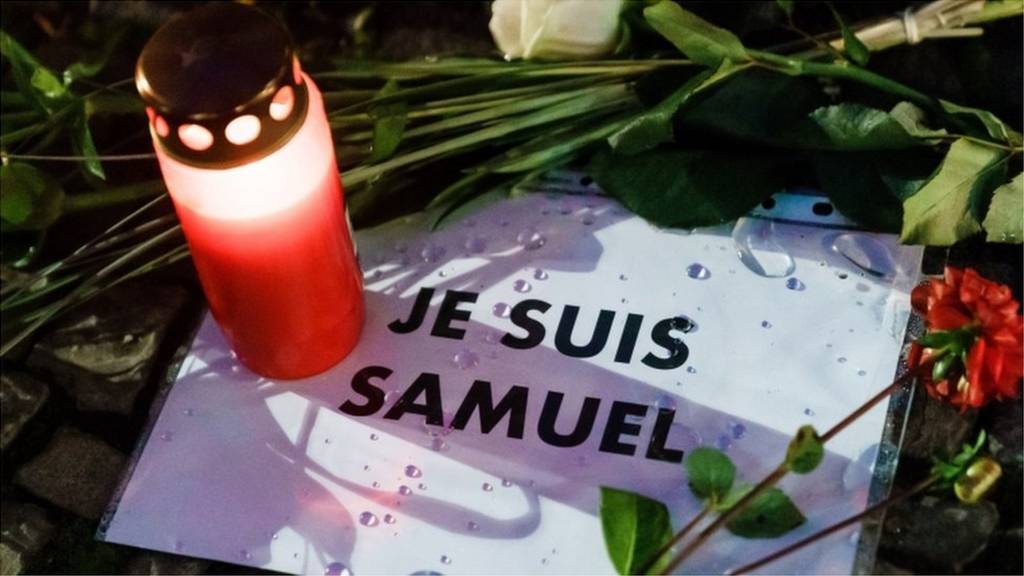 A candle and flowers are left next to a message in French that reads: "I am Samuel