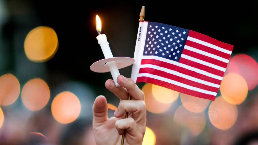A mourner holds up an American flag and a candle during a vigil for a fatal shooting at an Orlando nightclub, on 12 June 2016, in Atlanta