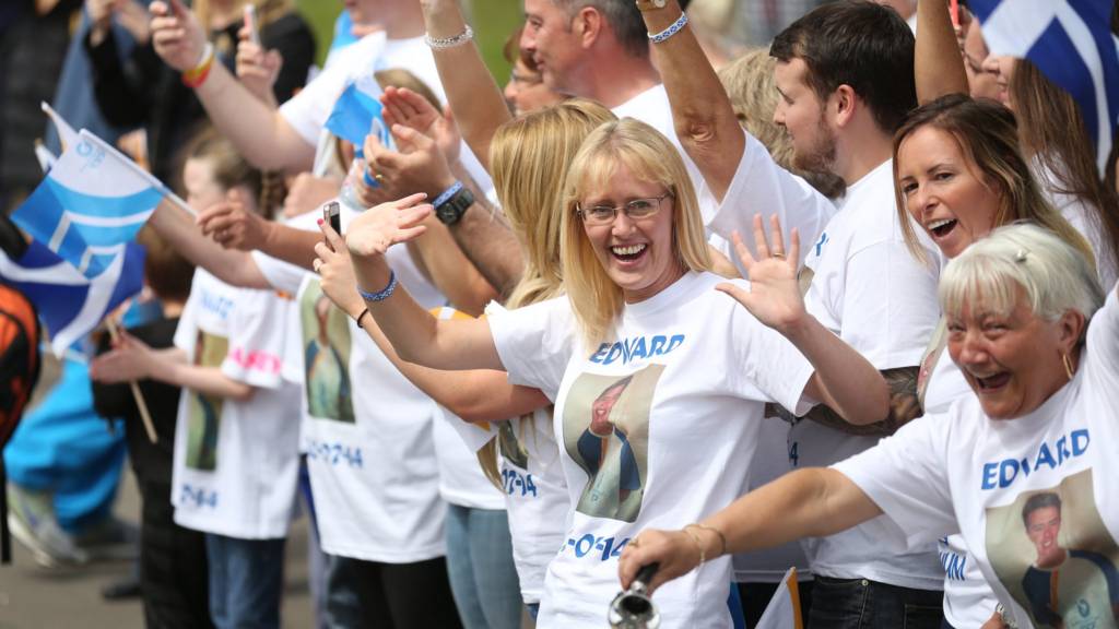 Supporters of Batonbearer 056 Edward Fitzpatrick wave as he carries the Glasgow 2014 Queen's Baton through Dennistoun in Glasgow.