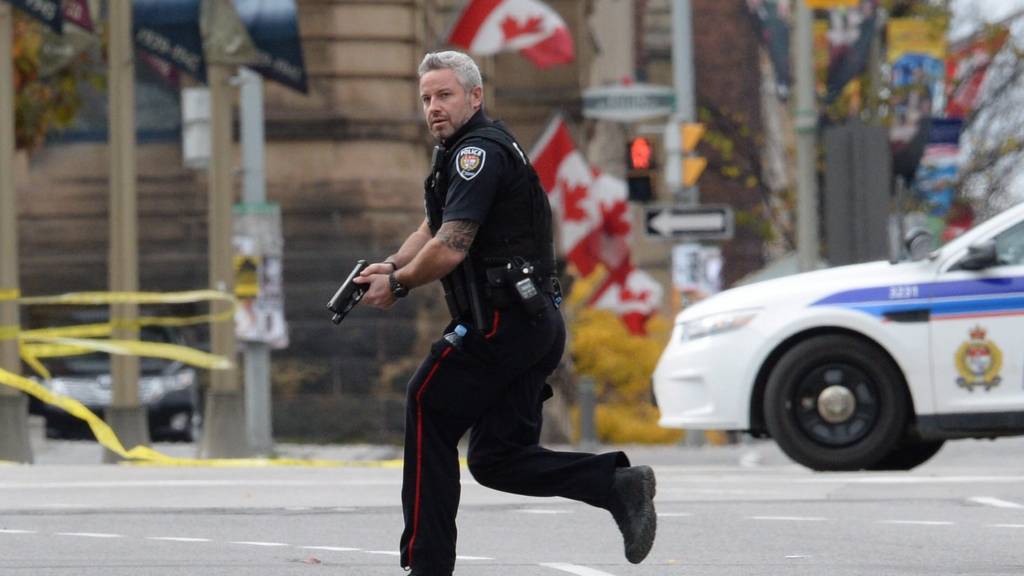 Police officer runs with weapon drawn outside parliament, Ottawa. 22 Oct 2014