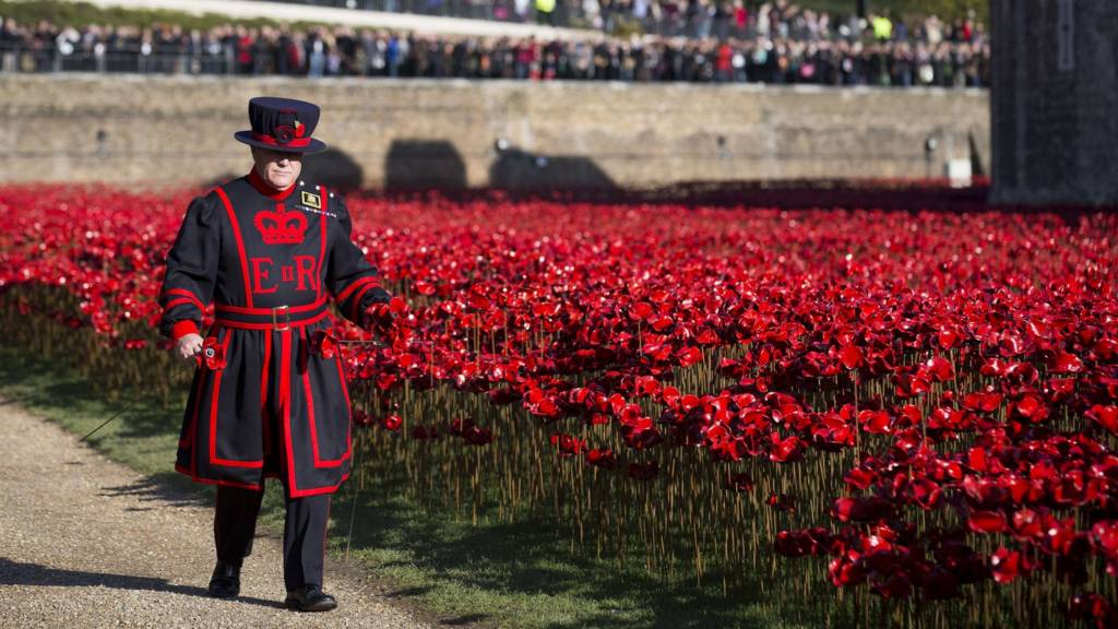 A Yeoman Warder walks past the "Blood Swept Lands and Seas of Red" installation