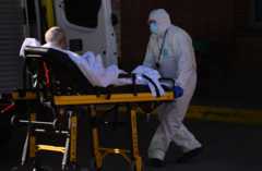 A hospital worker wheels a Madrid: coronavirus patient into a waiting ambulance to be taken to another sanitary center