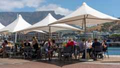 People eating and drinking under umbrellas on the waterfront with a backdrop of Table Mountain