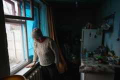 Женщина смотрит из окна своего разрушенного дома в Харькове