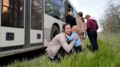 Μια γυναίκα κρατά ένα παιδί δίπλα σε ένα λεωφορείο καθώς πολίτες από τη Μαριούπολη ταξιδεύουν σε μια συνοδεία προς τη Ζαπορίζια