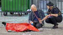 Сотрудница полиции успокаивает мужчину у трупа 13-летнего мальчика, погибшего в результате российского обстрела